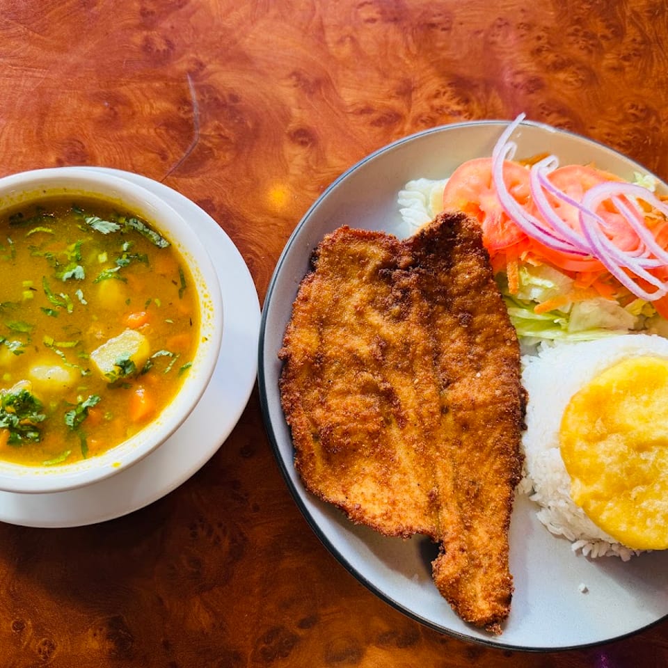 Fried fish with rice, salad, and a bowl of soup on a wooden table.