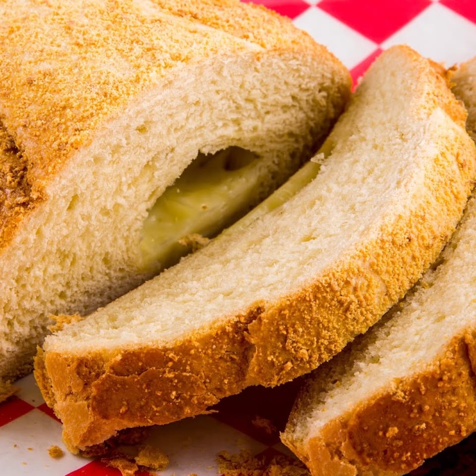 Sliced bread with a golden, crumbly crust and a creamy filling, on a red and white checkered paper.