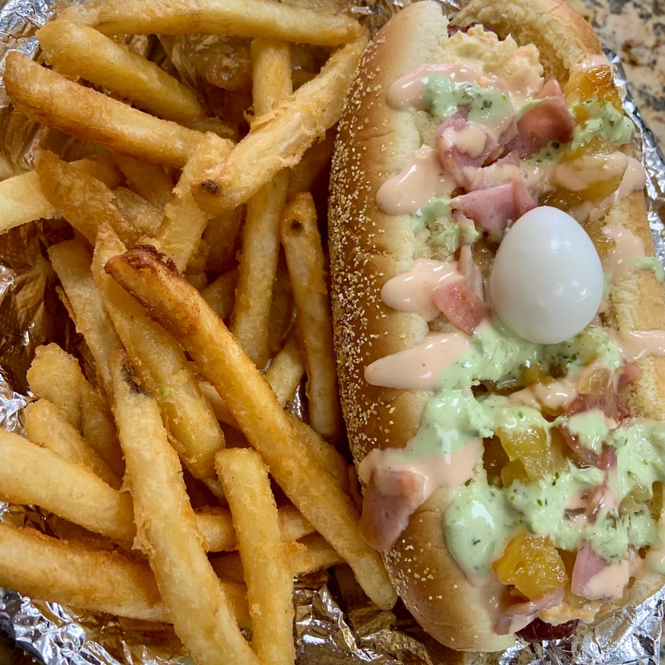 A hot dog with various toppings and a quail egg, served with a side of golden french fries.
