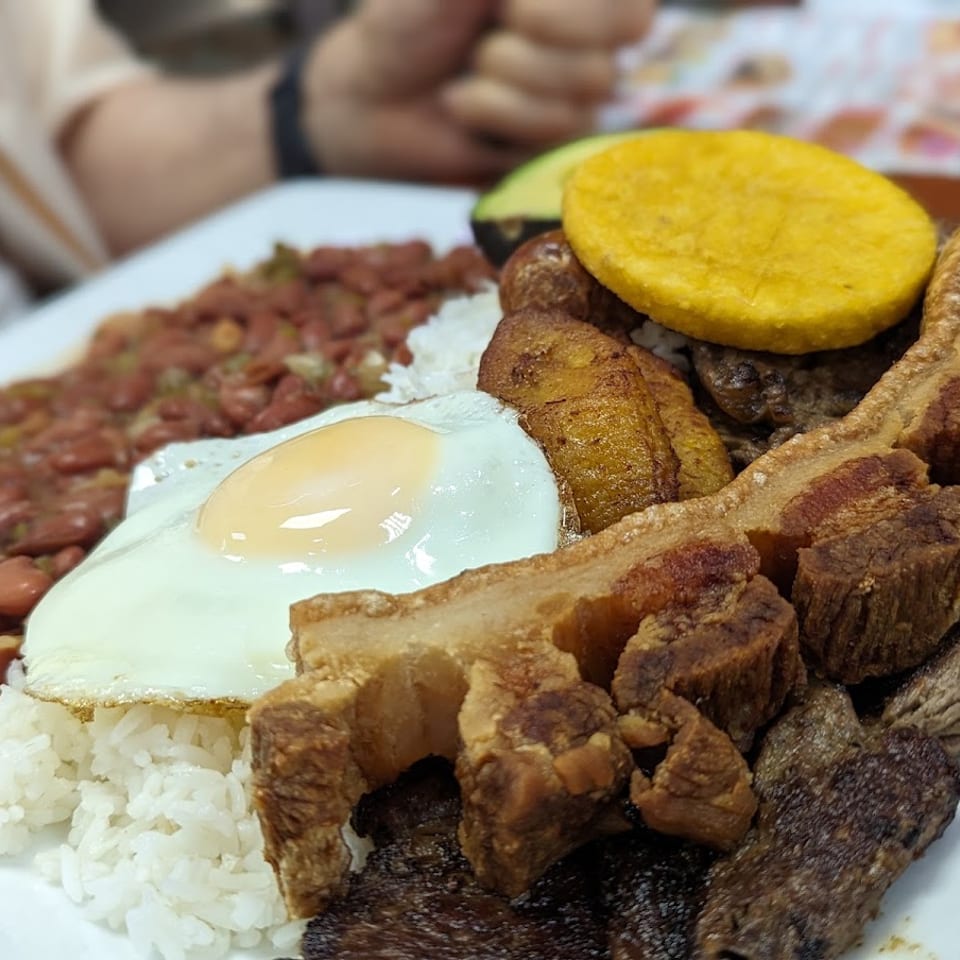 A large plate of Bandeja Paisa with rice, beans, fried egg, chicharron, plantain, and avocado.