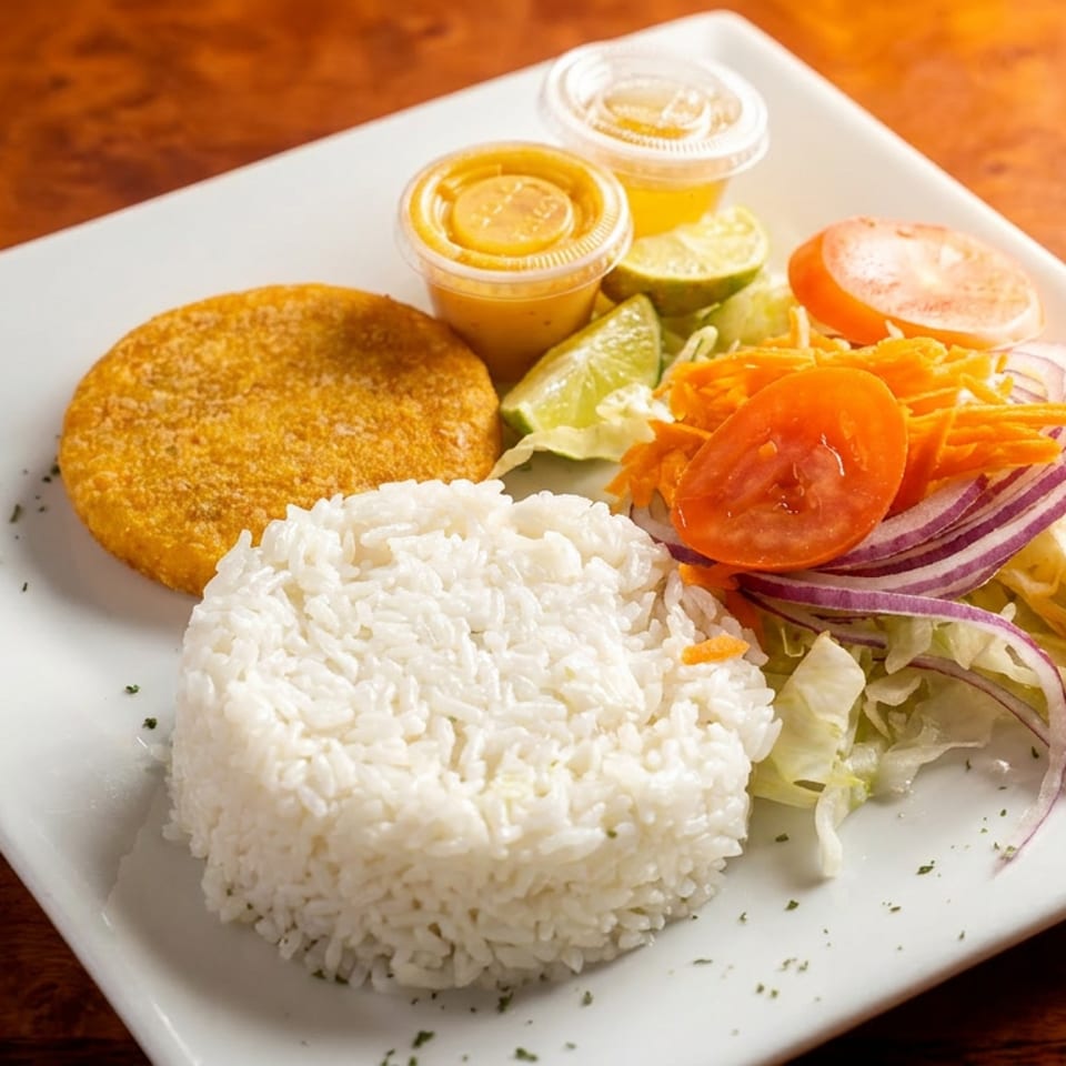 A white plate holds a golden-brown patty, white rice, a fresh salad, and two small sauce cups.